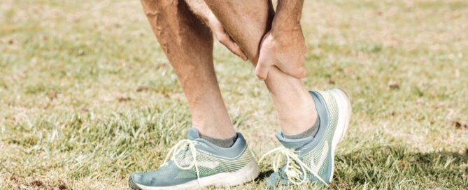 Man holding his calf in pain, wearing teal sneakers on green grass.