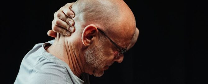 Side view of a man holding his neck in pain against a black background.